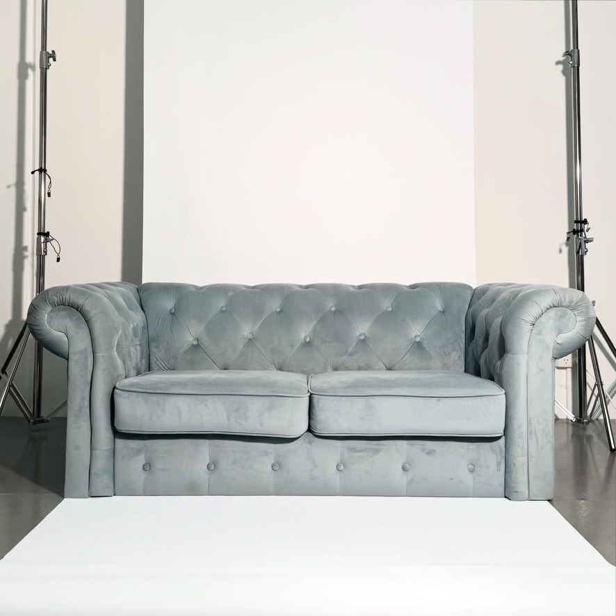 Powder blue velvet chesterfield two-seater between two chrome studio lighting stands.