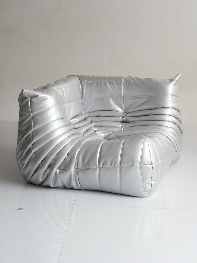 Silver Togo-style lounge chair, soft pleated metallic vinyl on a glossy white floor.