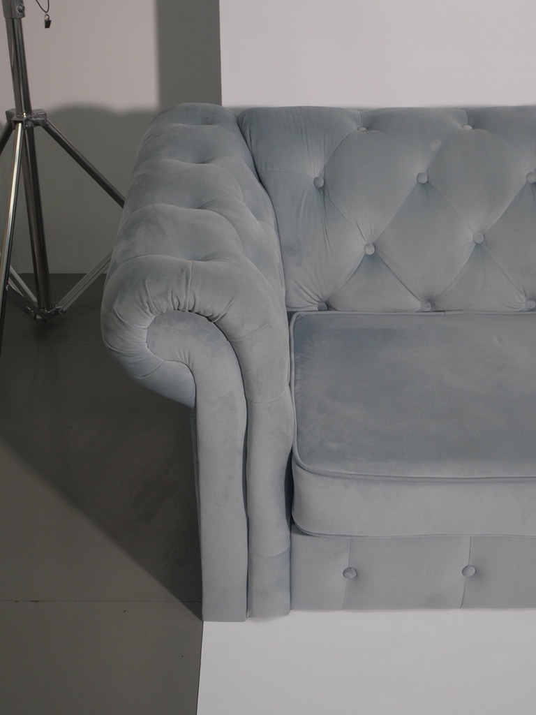 Close-up of the powder blue velvet chesterfield, button-tufted back and rolled arm.