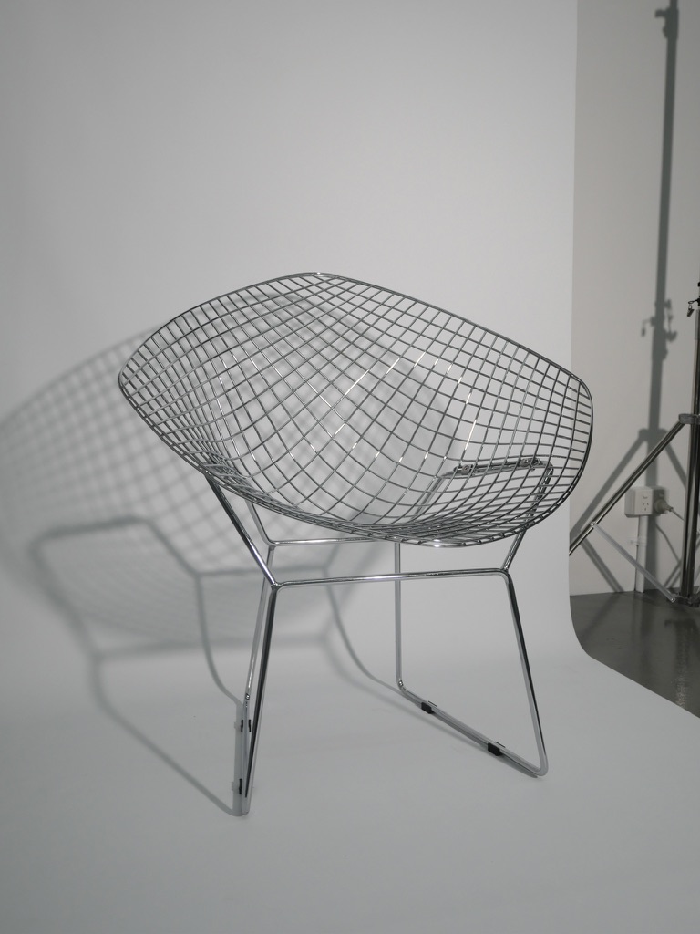 Chrome wire Bertoia diamond chair against a white wall.