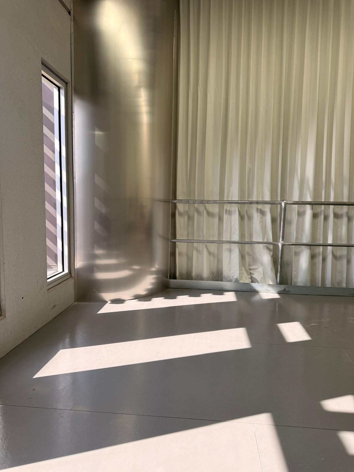 Sunlight pouring across polished concrete past block-out curtains and a stainless steel handrail.