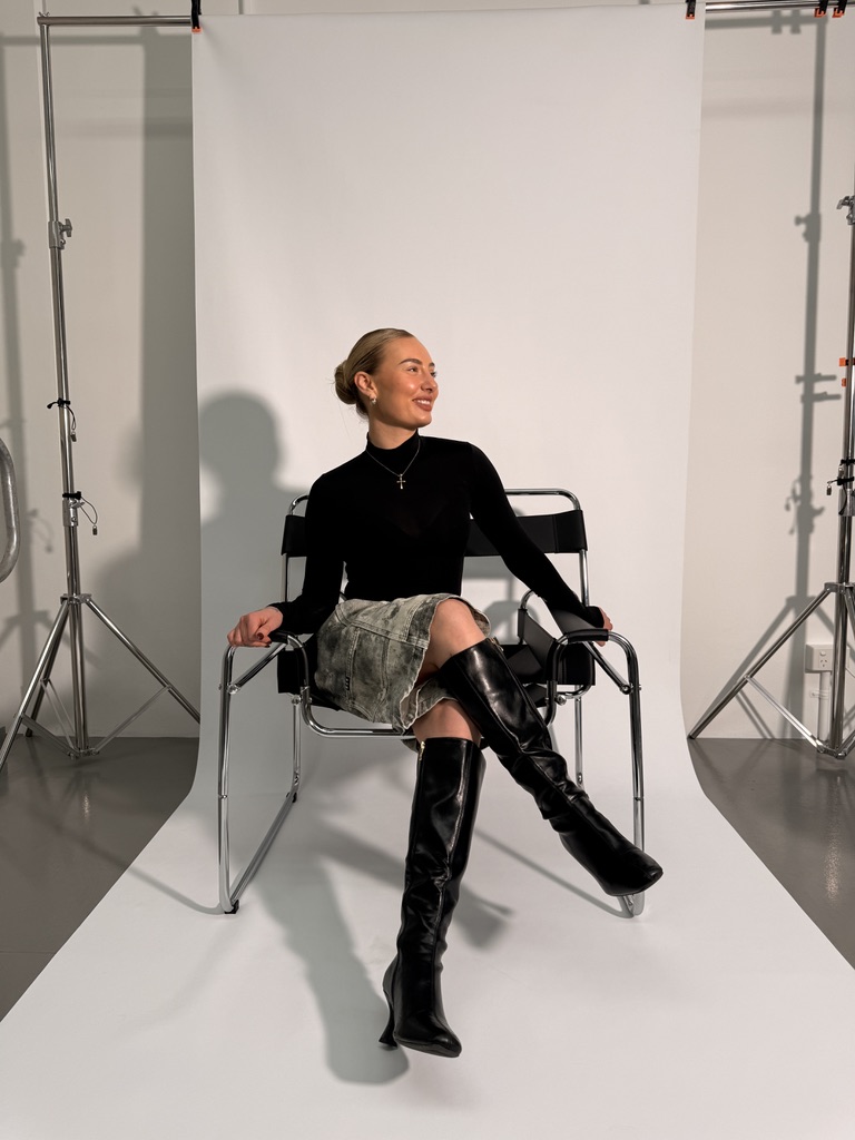 A model seated on the chrome and black Wassily chair on a white paper sweep, flanked by lighting stands.