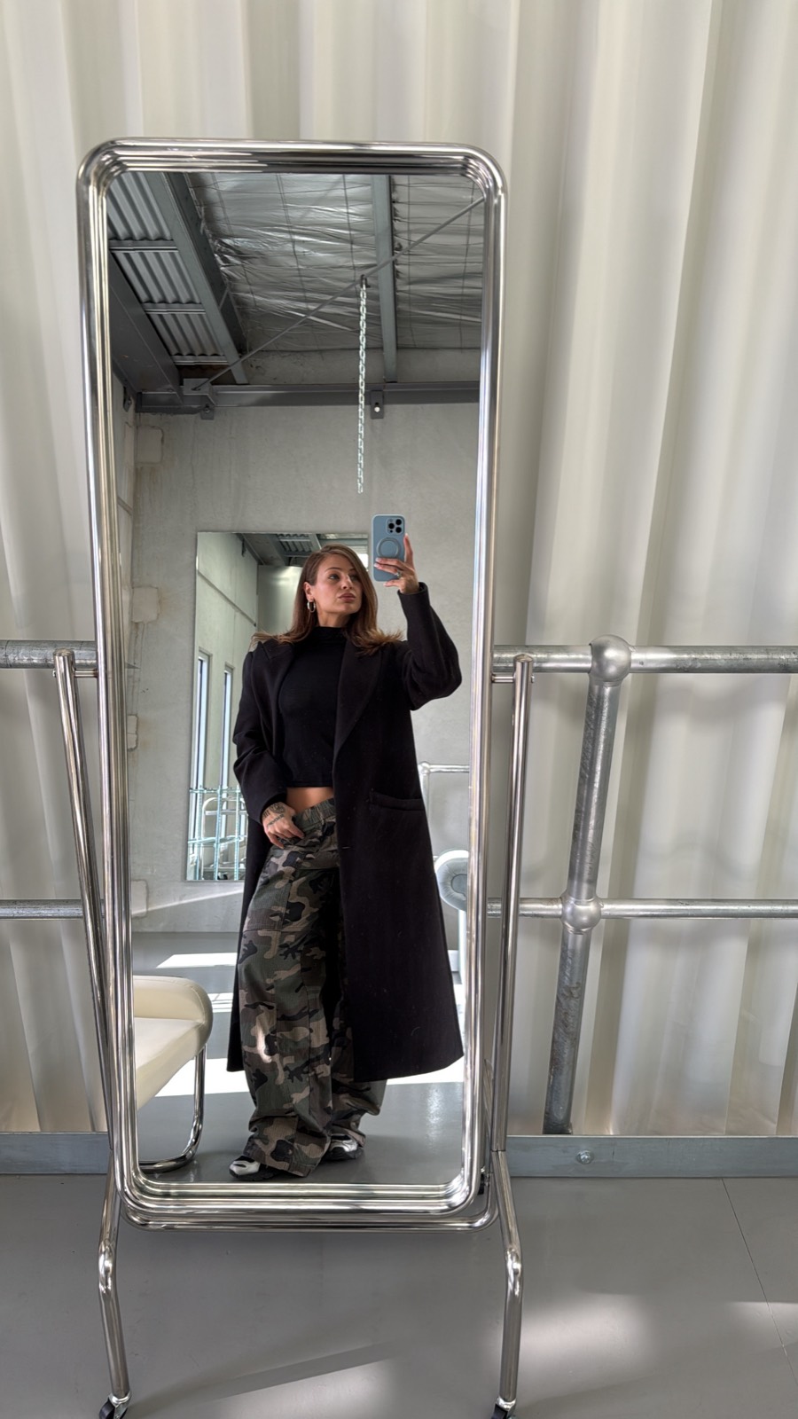 A visitor photographs themselves in the studio's freestanding floor mirror against the warehouse racking.