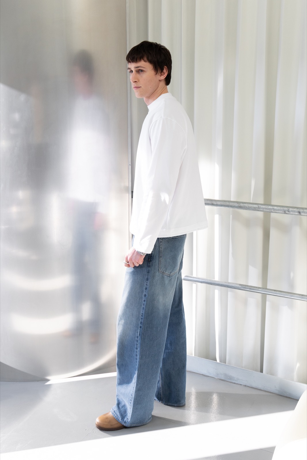 A model stands on the mezzanine between the frosted panels and chrome balustrade in bright natural light.