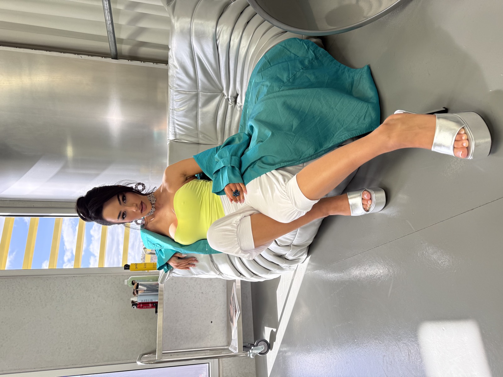 A model in teal reclines on the white lounge by the studio window.